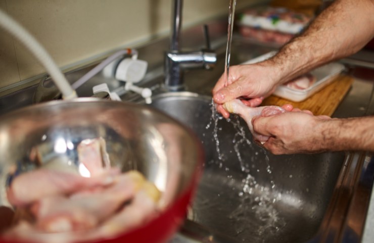 uomo che lava le cosce di pollo nel lavandino