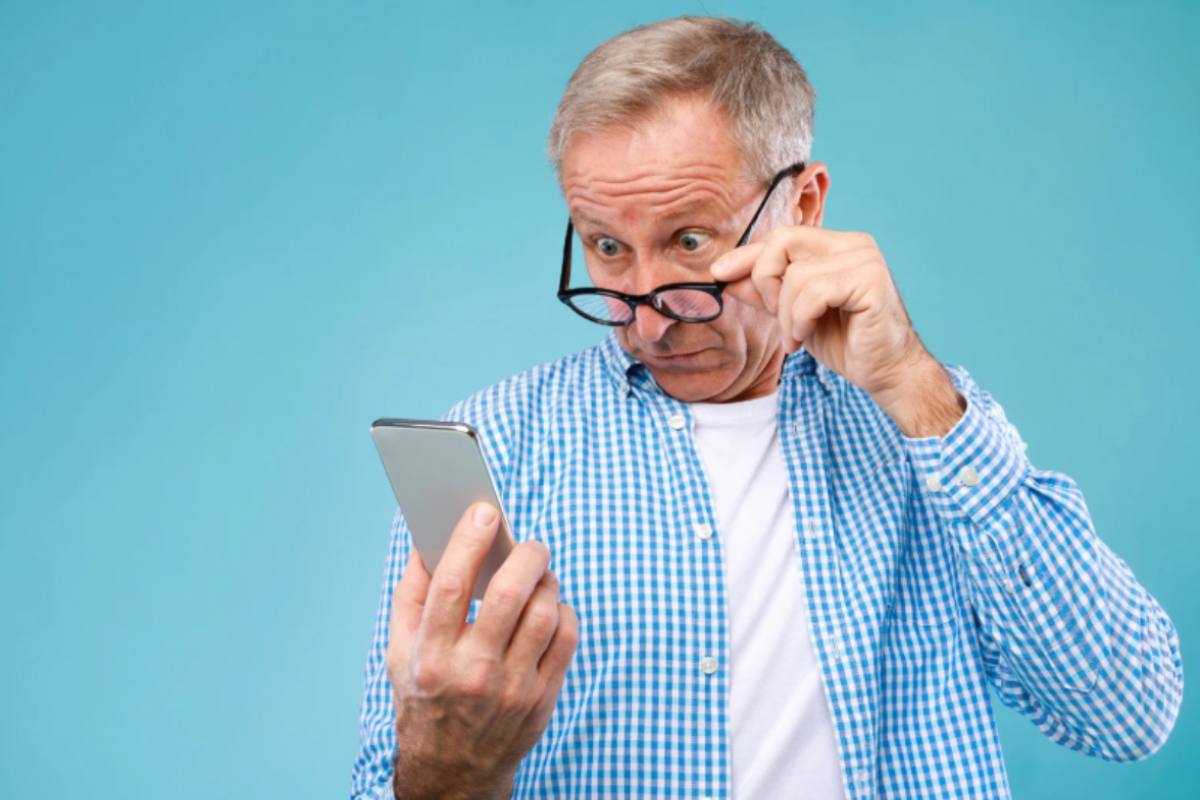 uomo anziano che guarda il cellulare con espressione incredula